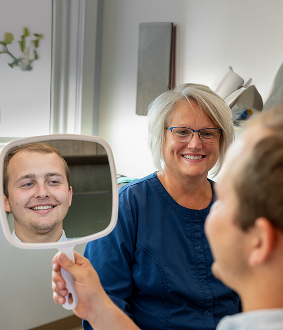 Team member watching patient check their smile in a handheld mirror