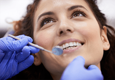 Tag: Woman smiling at dentist who is about to examine her mouth with gloved hands.