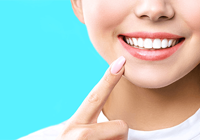 Nose-to-neck view of woman pointing to her perfect smile with light blue background.