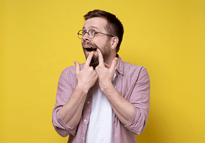 Man pointing to gap in his grin with yellow background.