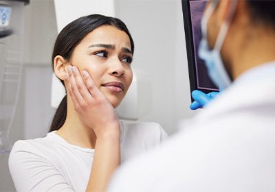 Woman holding hand to jaw in pain looking at X-ray with emergency dentist.